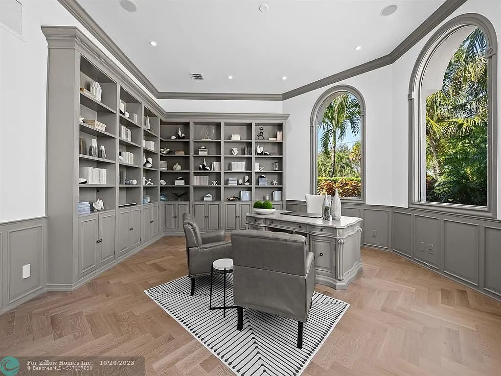 A home office with a desk , chairs , shelves and a large window.