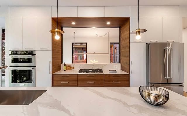 A kitchen with white cabinets , wooden cabinets , stainless steel appliances and a marble counter top.