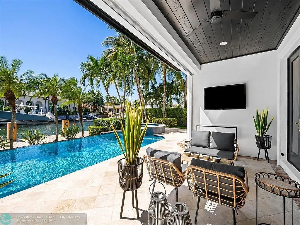 A patio with a couch , chairs , a television and a swimming pool.
