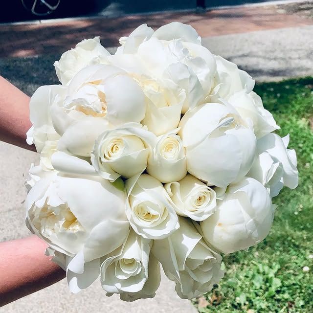 A person is holding a bouquet of white roses and peonies