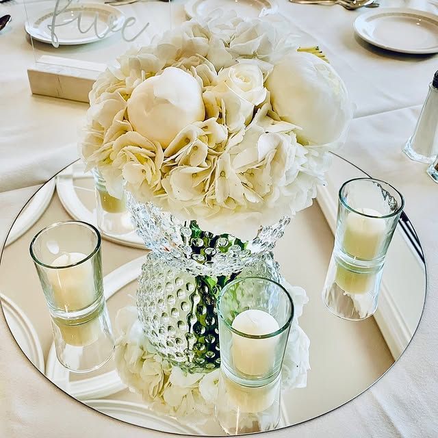 A round mirror with a vase of flowers and candles on it