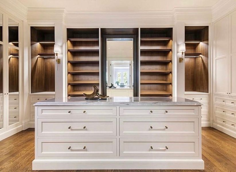 A walk in closet with lots of shelves and drawers and a large mirror