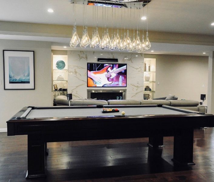 A pool table in a living room with a television on the wall