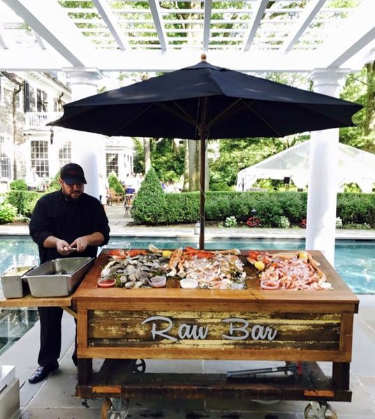 A chef prepares food at a raw bar in front of a pool
