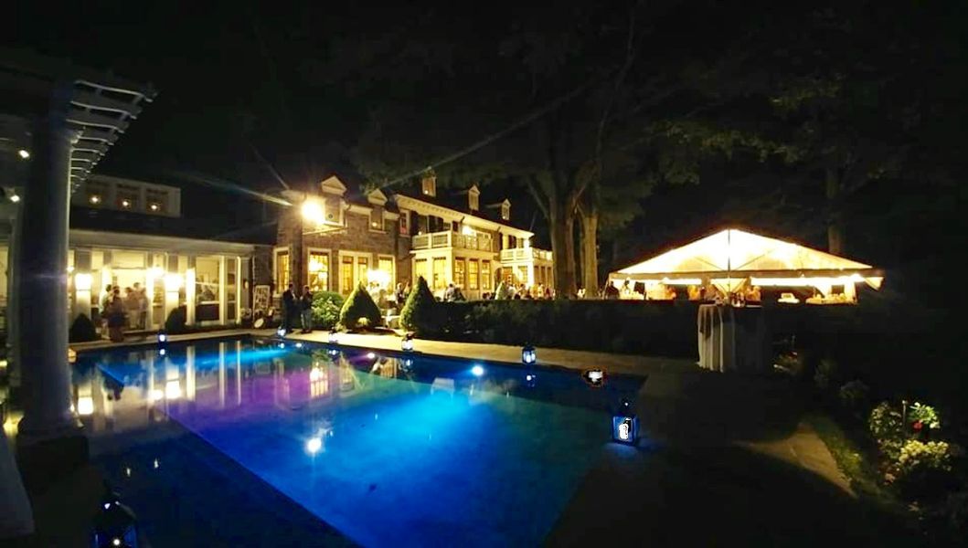 A large swimming pool is lit up at night in front of a house