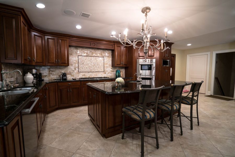 A kitchen with wooden cabinets, granite counter tops, stainless steel appliances and a large island