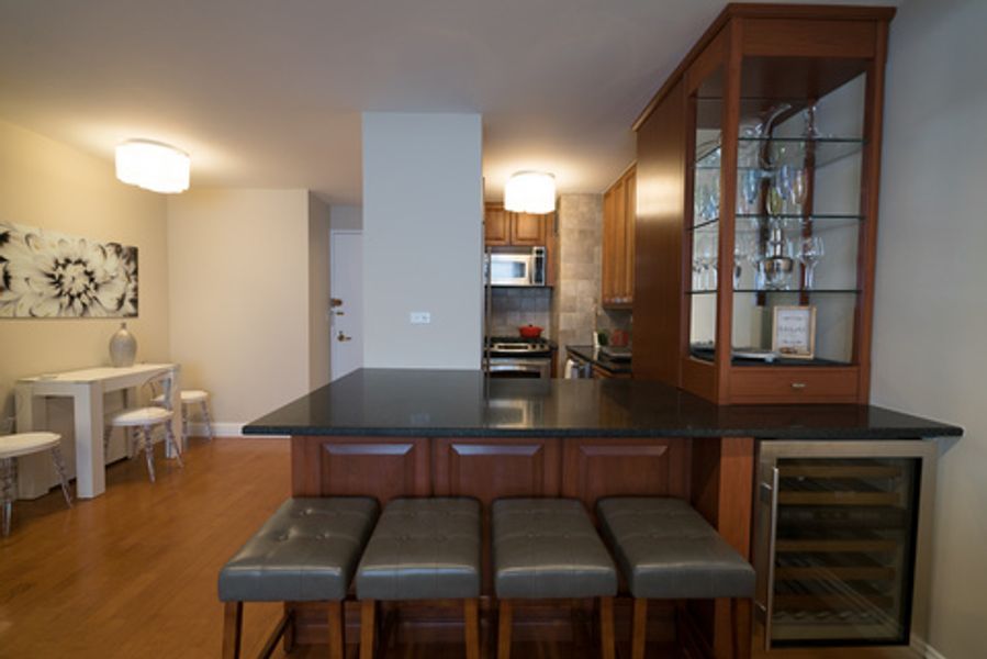 A kitchen with a bar and stools and a wine cooler