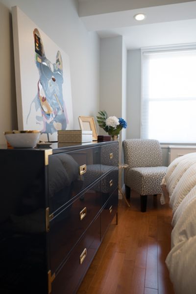 A bedroom with a dresser a chair and a painting on the wall
