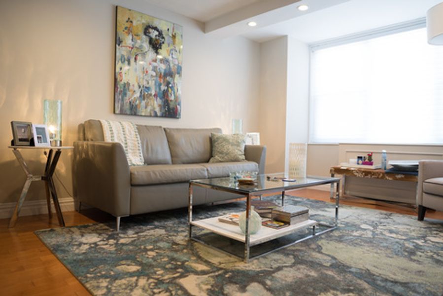 A living room with a couch, coffee table, chairs and a painting on the wall