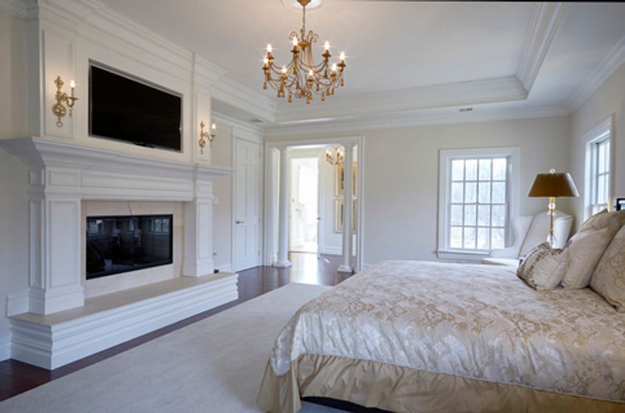 A bedroom with a bed, fireplace, television and chandelier