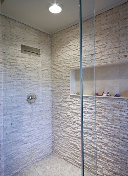 A walk in shower with a stone wall and a glass door