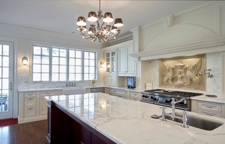 A kitchen with a large island, sink, stove and chandelier