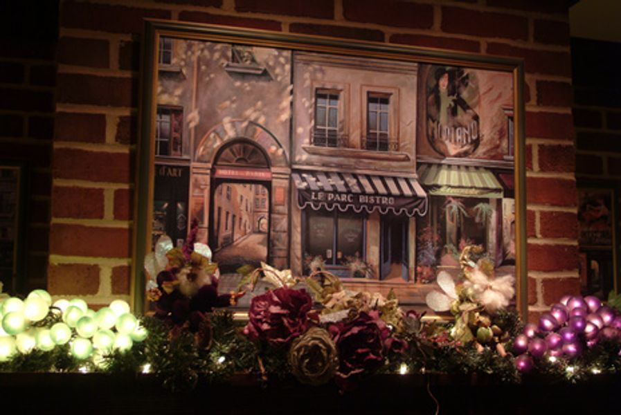 A framed painting of a brick building with flowers and christmas lights
