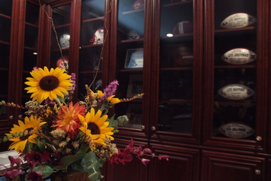A vase of sunflowers sits in front of a glass cabinet filled with footballs