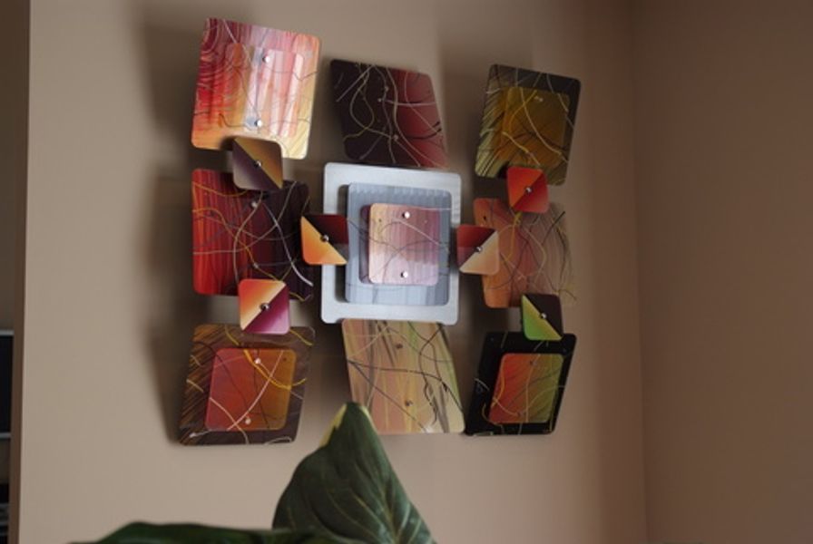 A colorful painting is hanging on a wall next to a plant