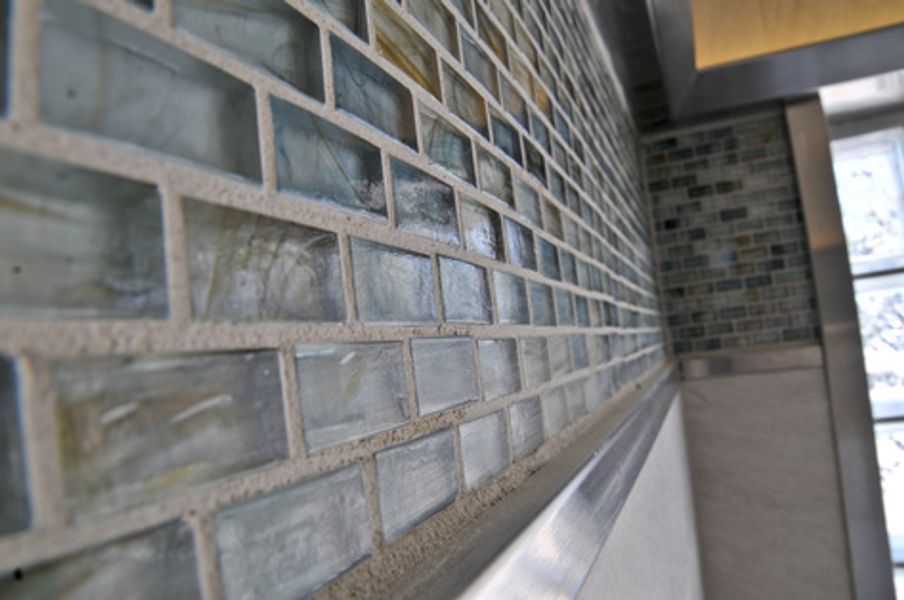 A close up of a brick wall with glass tiles and a stainless steel trim
