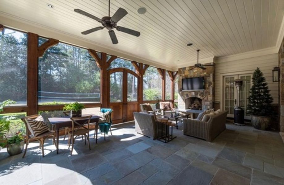 A screened in porch with a fireplace and a ceiling fan