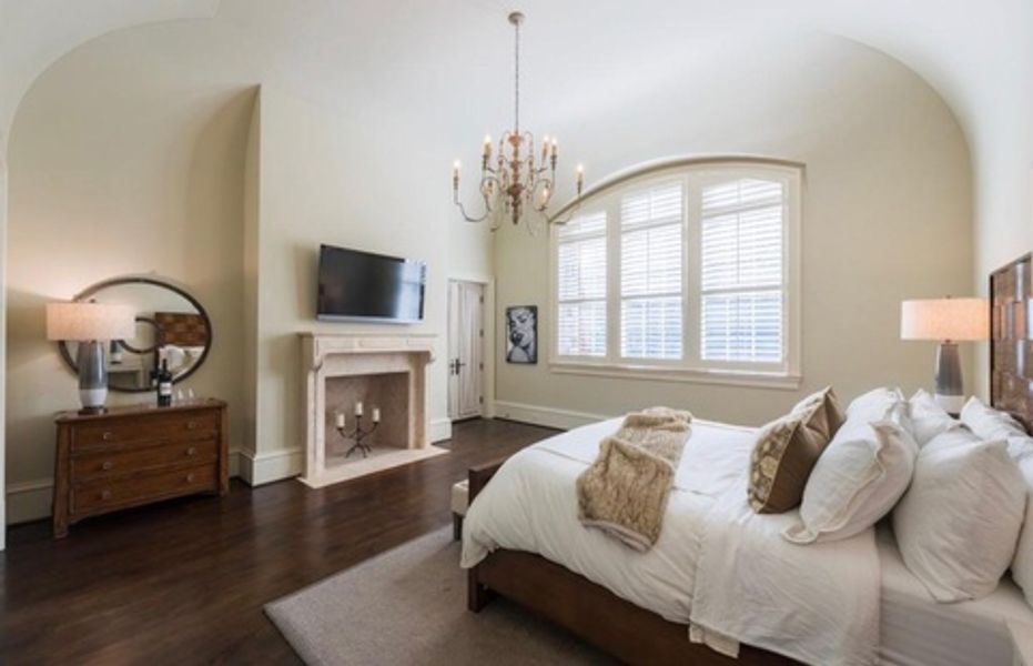 A bedroom with a bed, fireplace, television and dresser