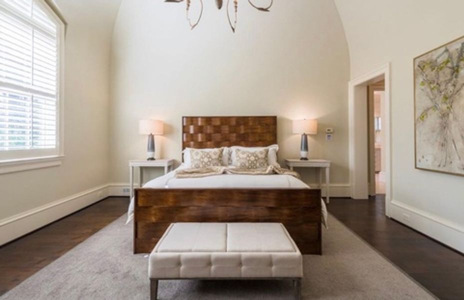 A bedroom with a bed, ottoman, lamps and a chandelier