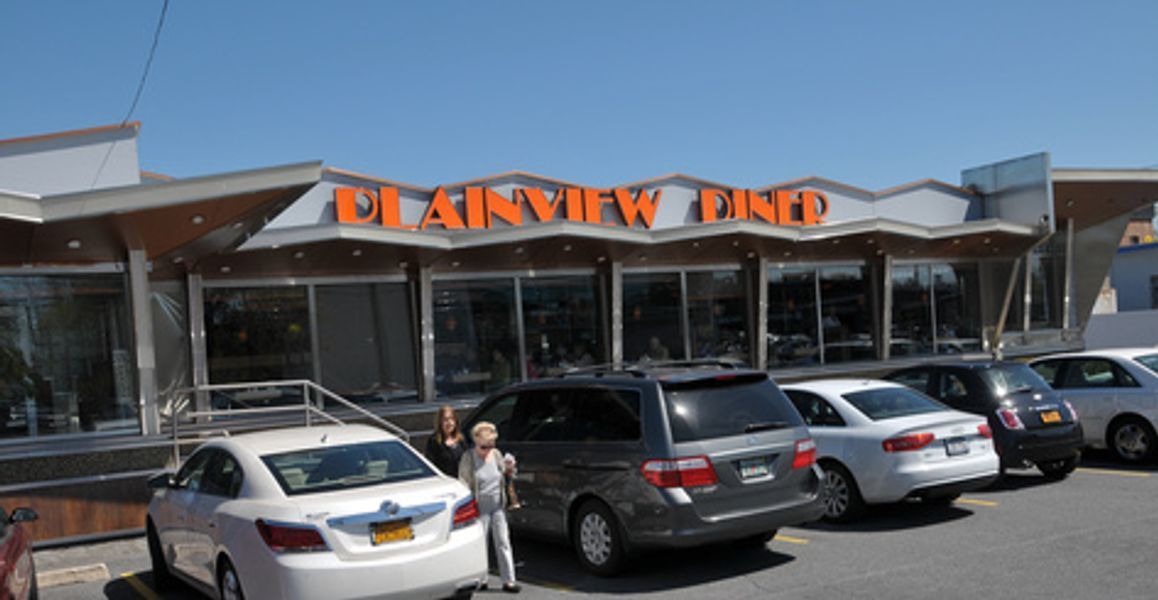 A row of cars are parked in front of a restaurant called plainview dino