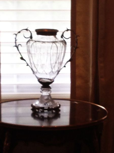 A glass vase sits on a table in front of a window