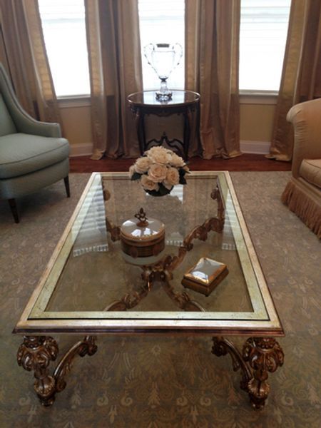 A glass coffee table in a living room with a vase of flowers on it