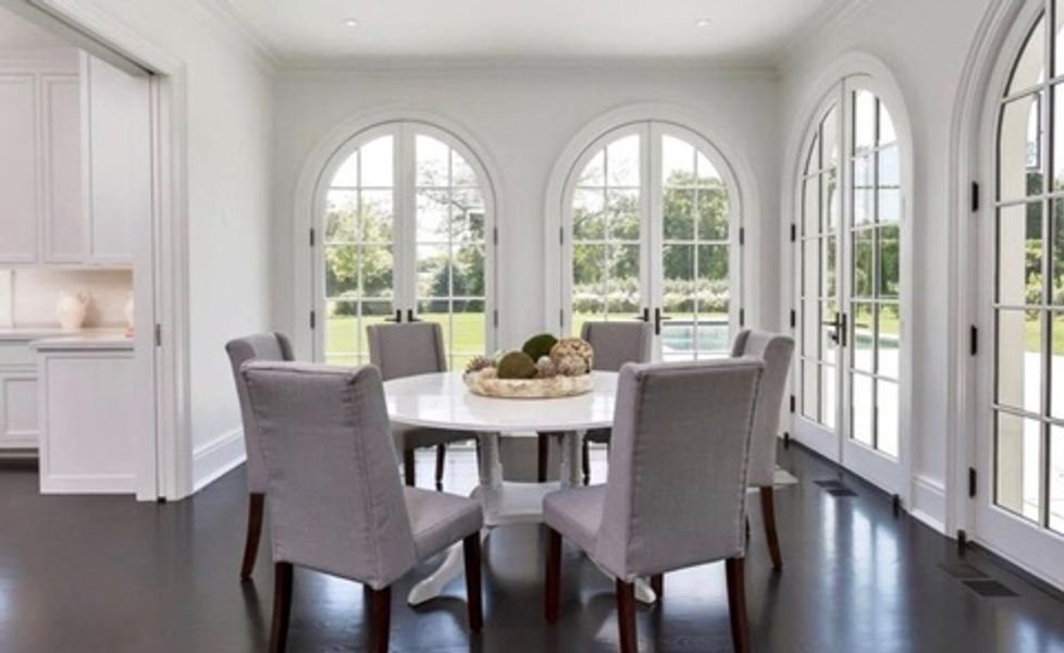A dining room with a round table and chairs and arched windows