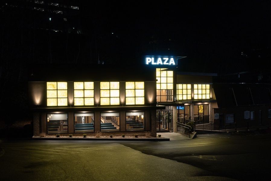 A restaurant called plaza is lit up at night