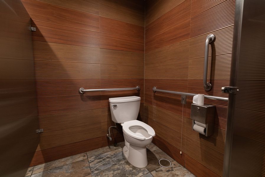 A bathroom with a toilet, handrails, and a paper towel dispenser