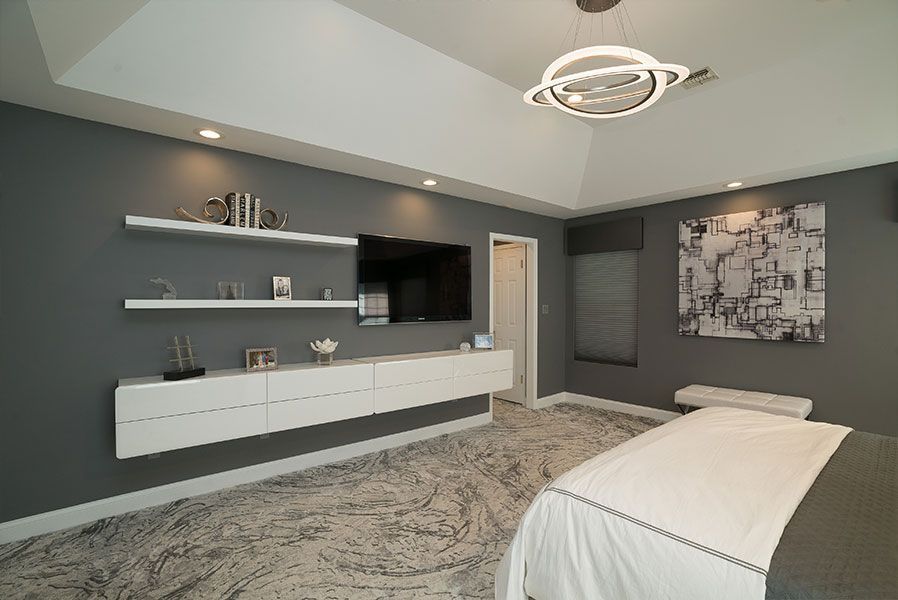 A bedroom with a bed, television, shelves and a chandelier