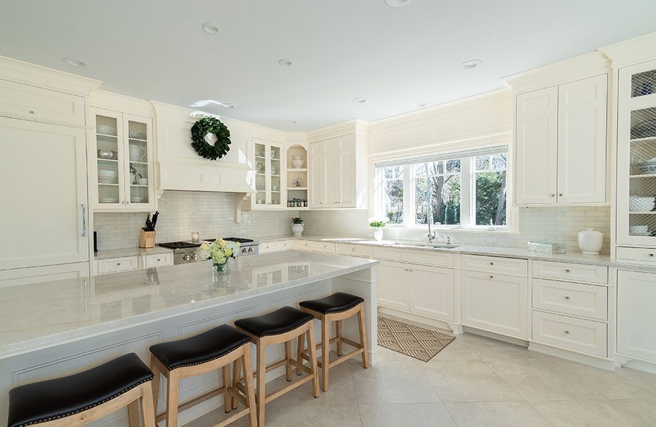 A kitchen with white cabinets, granite counter tops, and stools