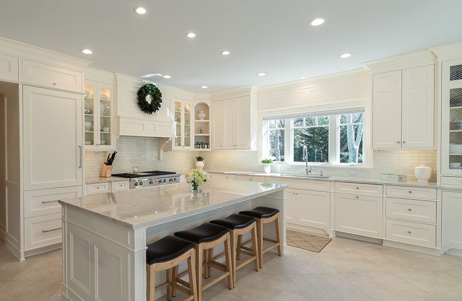 A kitchen with white cabinets, granite counter tops, stools and a large island
