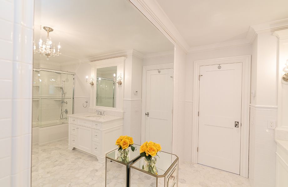 A bathroom with white cabinets, a sink, a mirror and a table with flowers on it