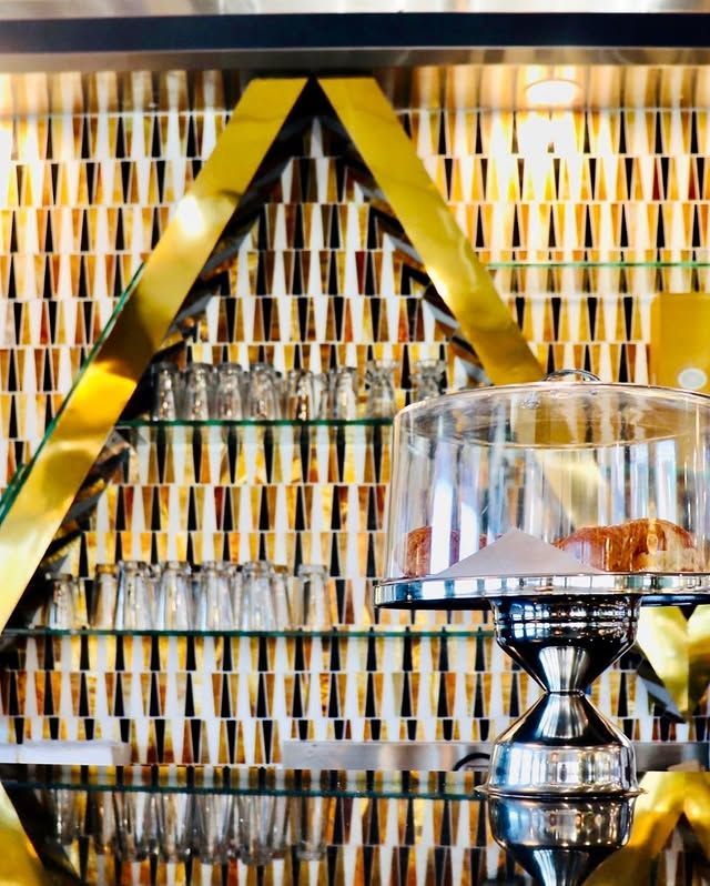 A glass display case with a cake on top of it in front of a gold wall.