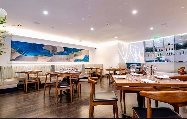 A restaurant with tables and chairs and a large painting on the wall.