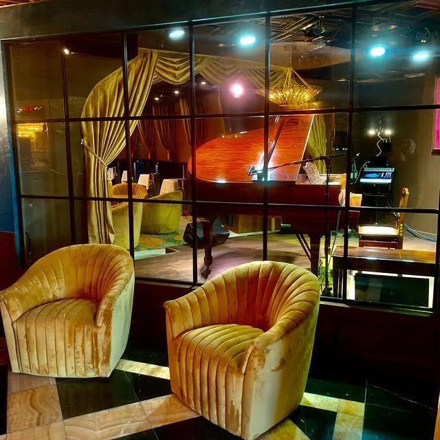 Two chairs in front of a window with a piano in the background