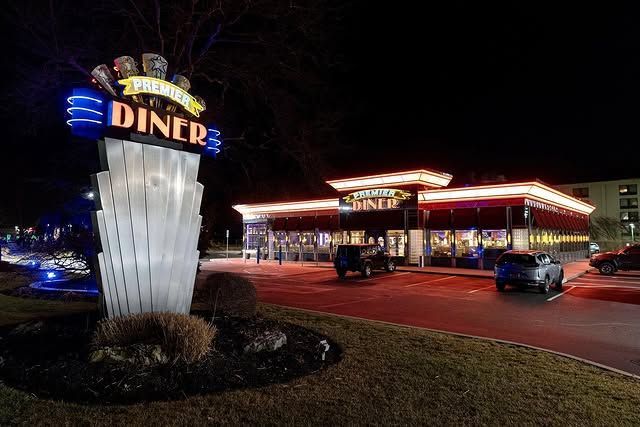 A diner is lit up at night with cars parked in front of it.