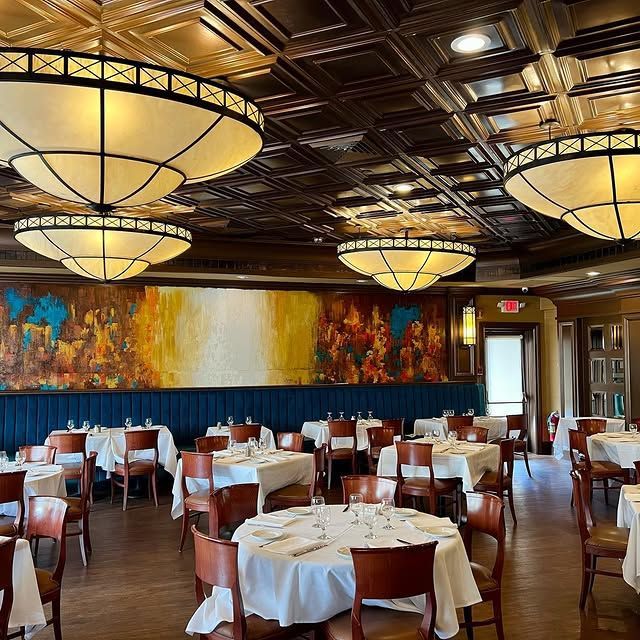 A restaurant with tables and chairs and a large painting on the wall