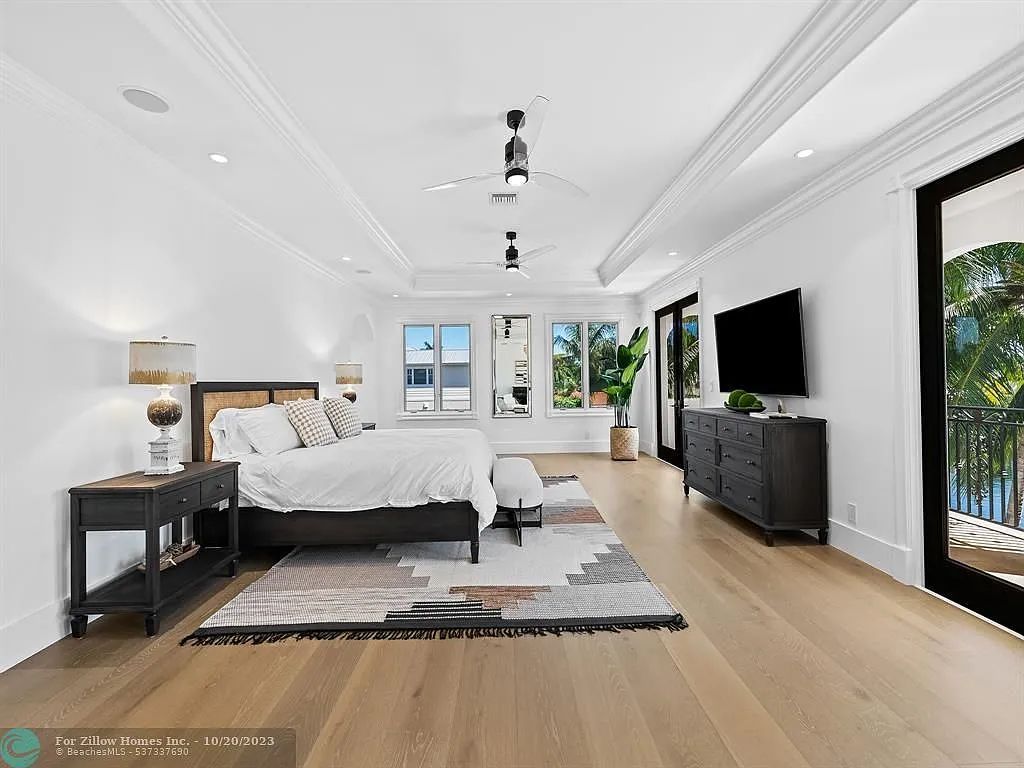 A large bedroom with hardwood floors , a bed , a television and a balcony.