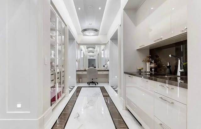 A long hallway in a house with white cabinets and marble floors.