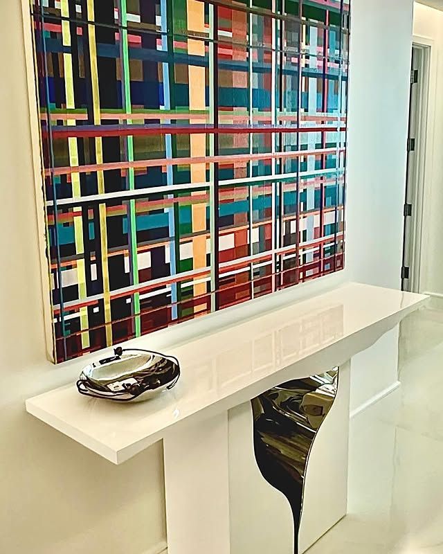 A colorful painting hangs above a white table in a hallway