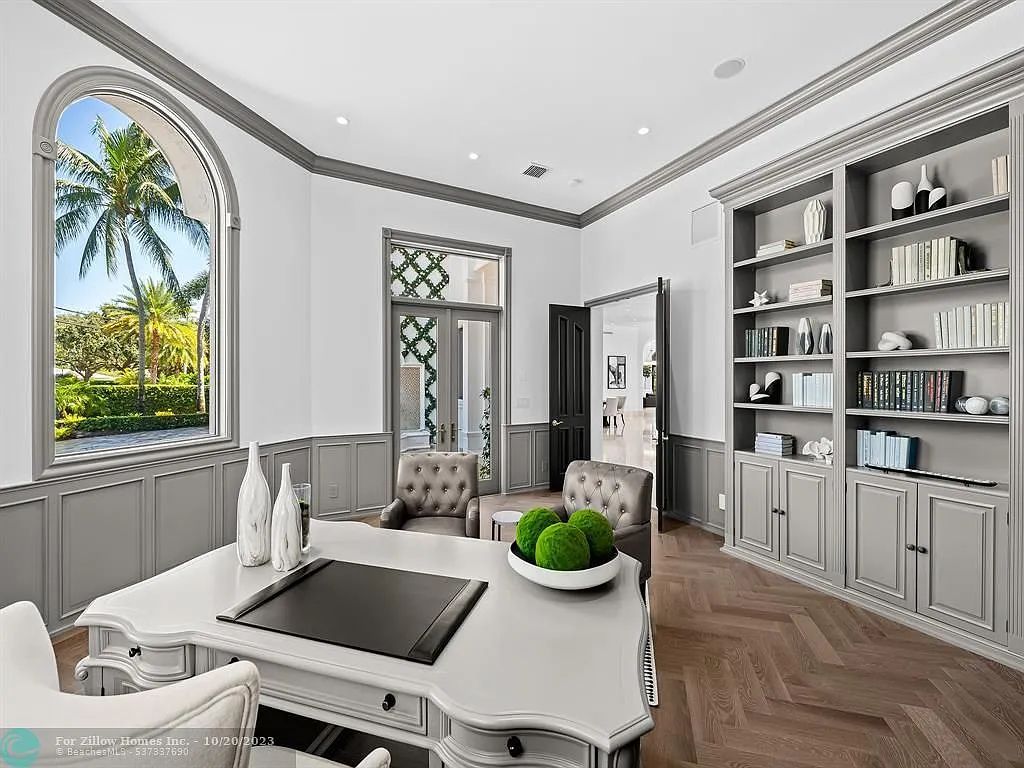 A home office with a desk , chairs , shelves and a large window.