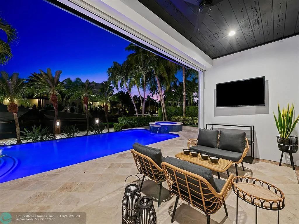 A patio with a couch , table , and television overlooking a swimming pool.