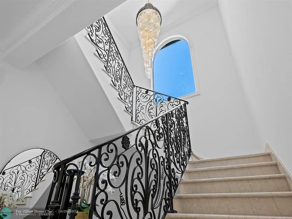 A staircase with a wrought iron railing and a chandelier hanging from the ceiling.