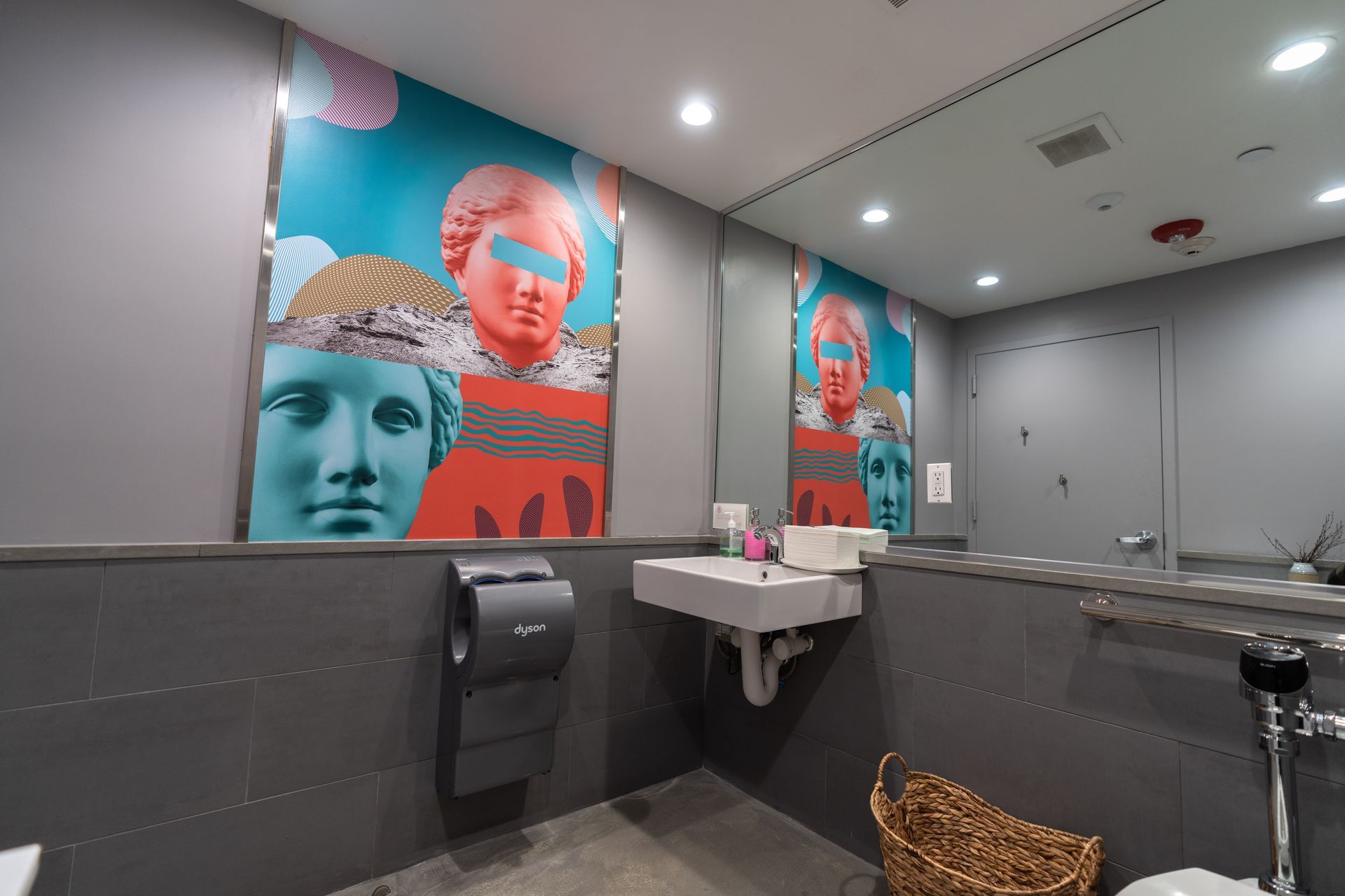 A bathroom with a sink , toilet , mirror and paintings on the wall.