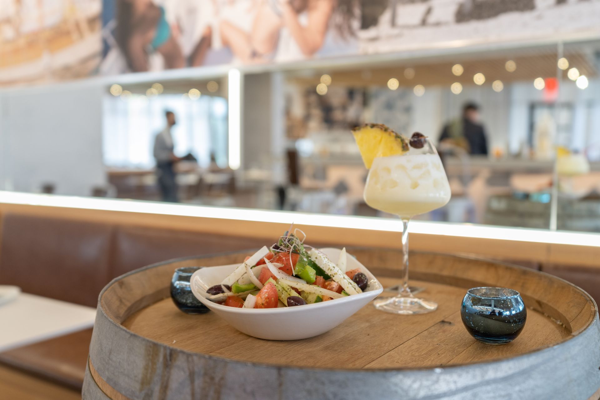A bowl of salad and a drink are on a wooden barrel.