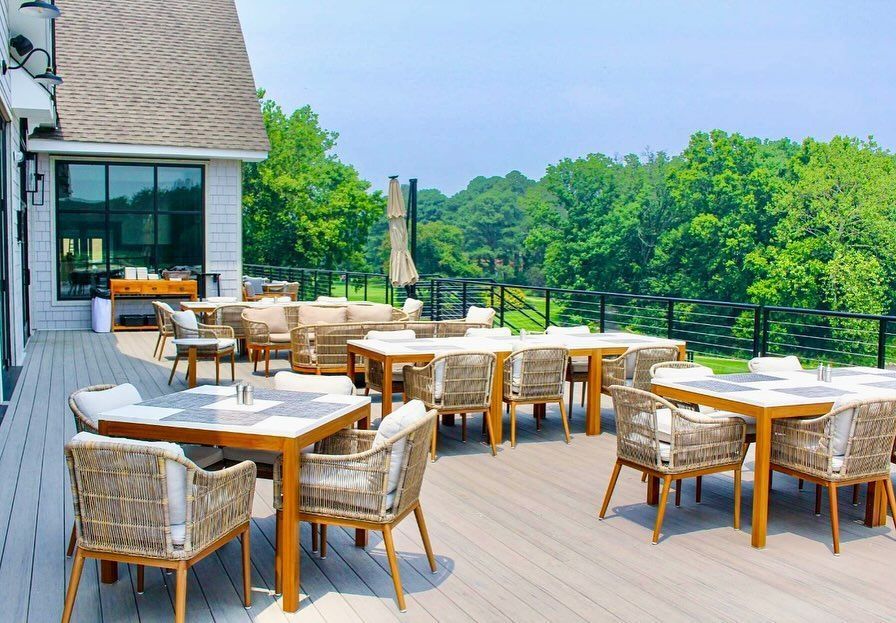 There are many tables and chairs on the deck of a restaurant.