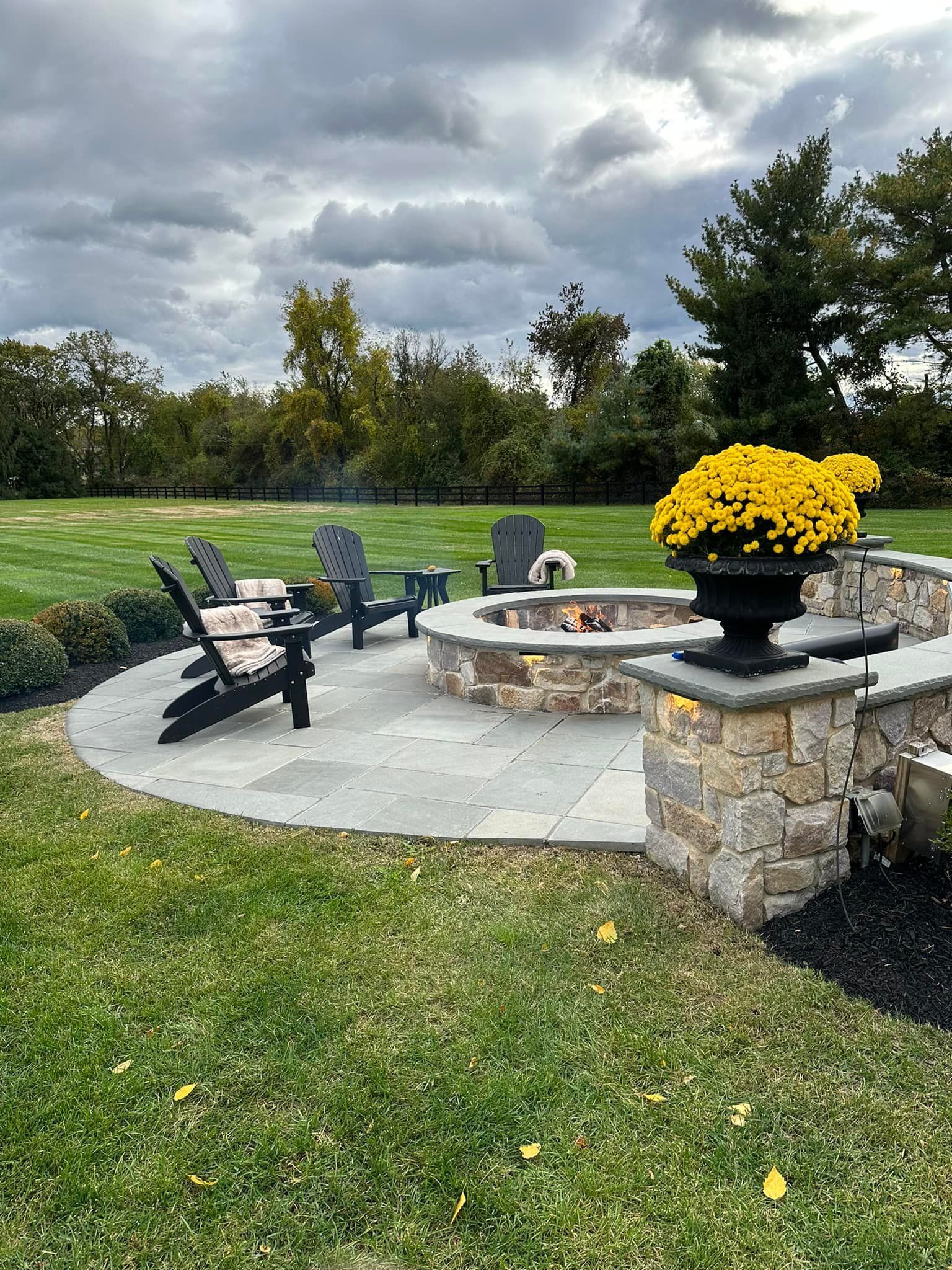 There is a fire pit in the middle of the yard with chairs around it.