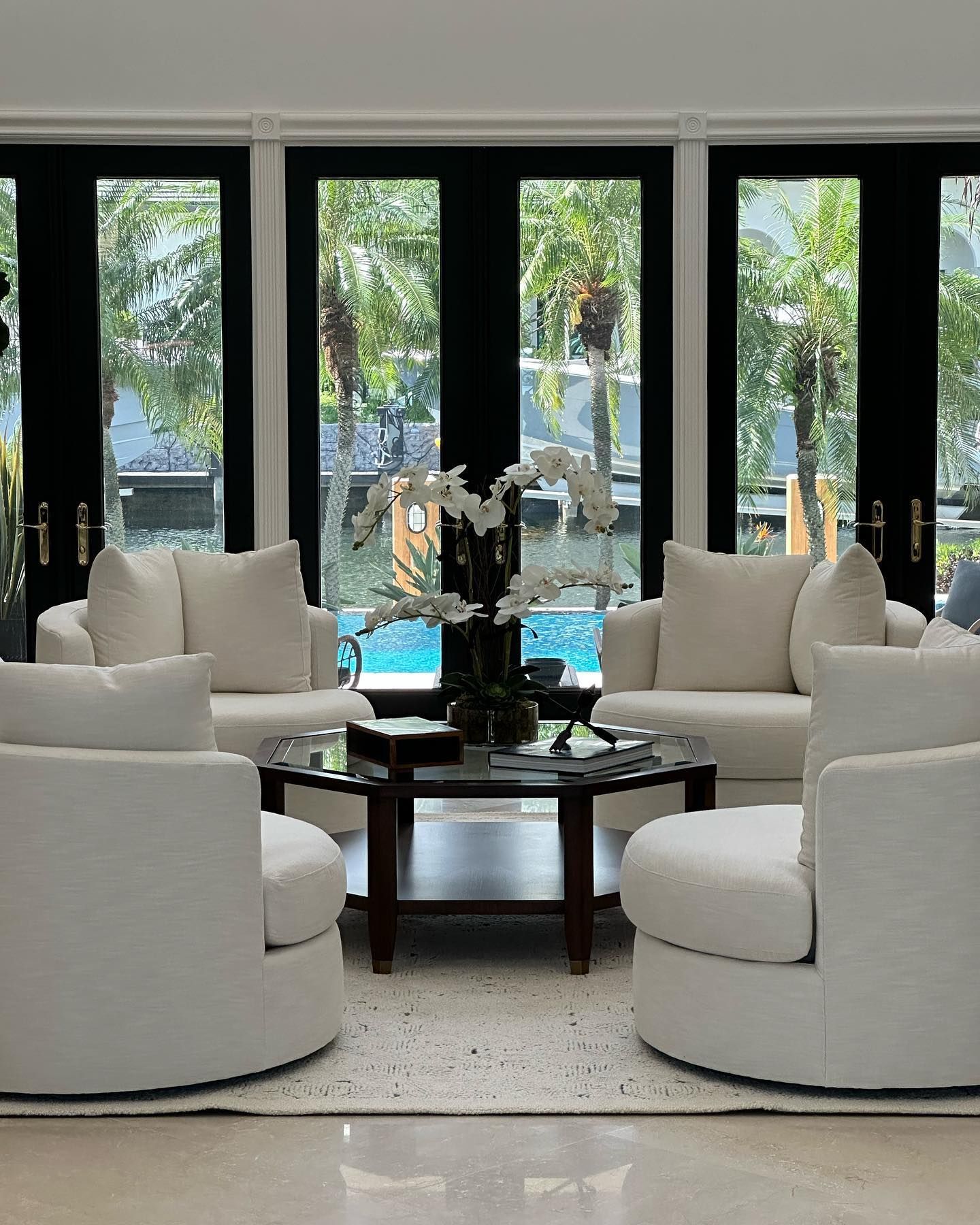 A living room with white furniture and a swimming pool in the background