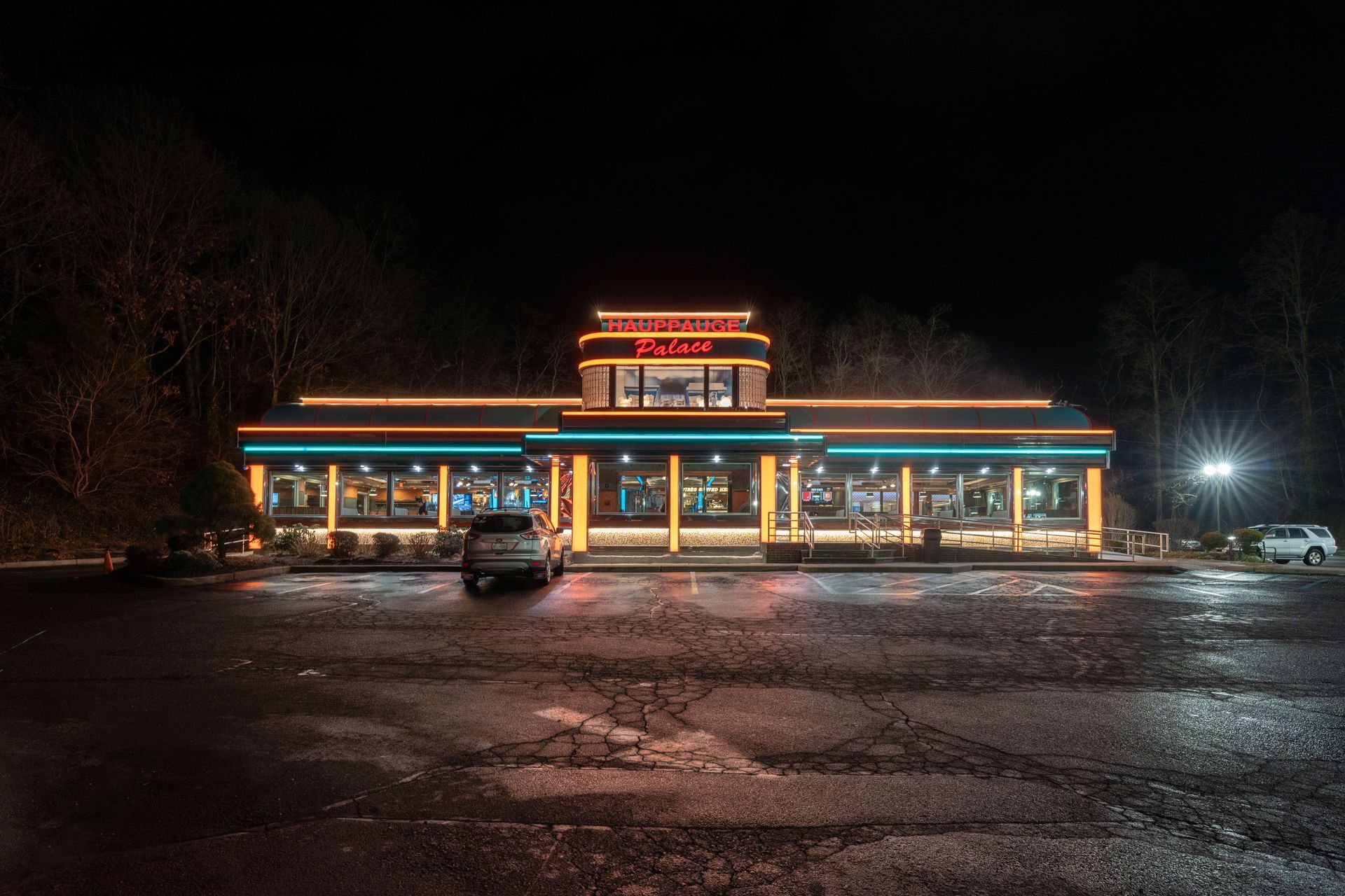 A diner is lit up at night with cars parked in front of it.